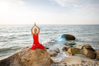 Pratik yoga taş gündoğumu deniz kenarında, Kırmızı elbiseli bir kadın