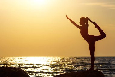 Pratik yoga taş gündoğumu deniz kenarında, Kırmızı elbiseli bir kadın