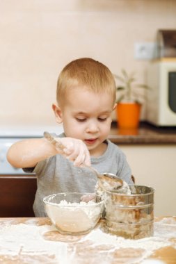 Küçük çocuk çocuk anne Noel ışık mutfakta zencefilli bisküvi pişirmek için yardımcı olur. Gri T-shirt hafta sonu sabah evde masada demir elek ve un ile 2-3 yıl içinde mutlu sarışın çocuk.