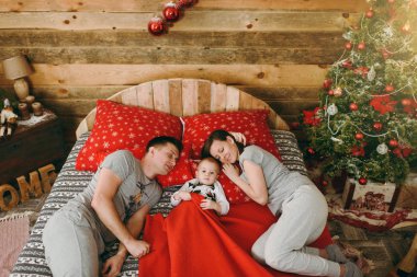 Mutlu anne Noel ağacı yakınındaki yatak odasında bir şekilde dekore edilmiş yeni yıl ahşap evde kırmızı oyuncaklar ile yatan küçük çocuk çocuk ile. Yaşam tarzı, Aile ve tatil 2018 kavramı. Baba, anne ve oğlu