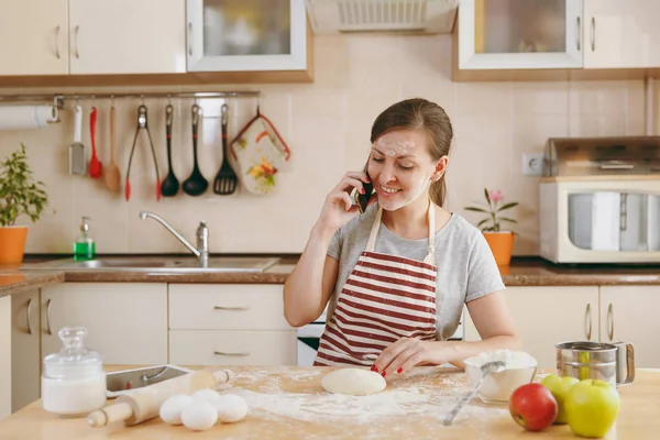 Μια νεαρή όμορφη ευτυχισμένη γυναίκα κάθεται σε ένα τραπέζι με αλεύρι και πρόκειται να προετοιμάσει ένα χριστουγεννιάτικο κέικ στην κουζίνα. Μαγείρεμα σπίτι. Προετοιμασία φαγητού. — Φωτογραφία Αρχείου
