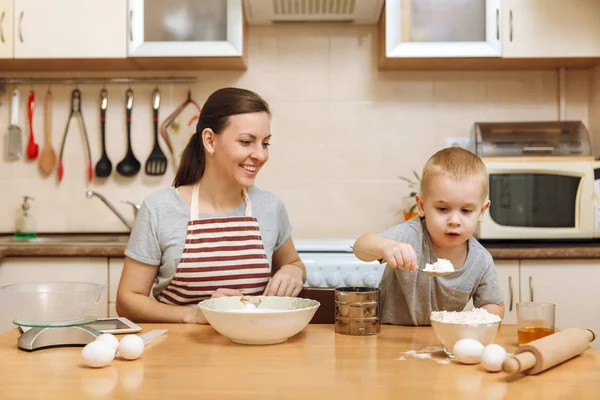 Little kid boy helps mother to cook Christmas ginger biscuit in light kitchen with tablet on the table. Happy family mom 30-35 years and child 2-3 in weekend morning at home. Relationship concept — Stock Photo, Image