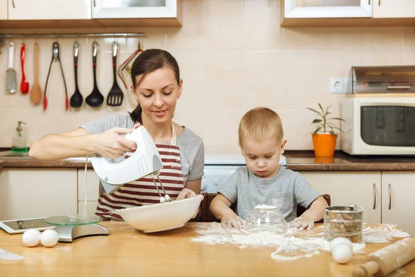 Liten unge pojke hjälper mamma att laga jul ingefära kex i ljust kök med tablett på bordet. Lycklig familj mamma 30-35 år och barn 2-3 i helgen morgon hemma. Relation-konceptet — Stockfoto