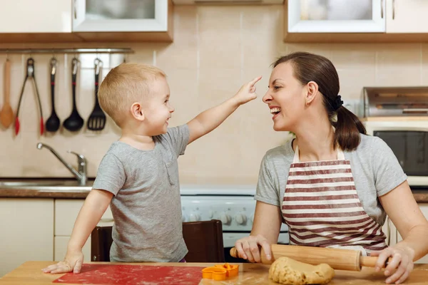 Little kid boy helps mother to cook Christmas ginger biscuit in light kitchen. Happy family mom 30-35 years and child 2-3 roll out dough and cut out cookies at home. Relationship and love concept — Stock Photo, Image