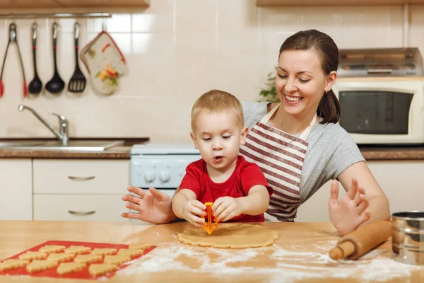 Little kid boy helps mother to cook Christmas ginger biscuit in light kitchen. Happy family mom 30-35 years and child 2-3 roll out dough and cut out cookies at home. Relationship and love concept — Stock Photo, Image