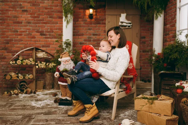 Τρυφερός νεαρός ευτυχισμένη μητέρα με χαριτωμένο μικρό παιδί αγόρι ντυμένο με πουλόβερ που κάθεται σε καρέκλα με Santa στο διακοσμημένο δωμάτιο στο σπίτι με το νέο έτος. Χριστούγεννα καλή διάθεση. Τρόπου ζωής, οικογένεια και διακοπές έννοια 2018 — Φωτογραφία Αρχείου