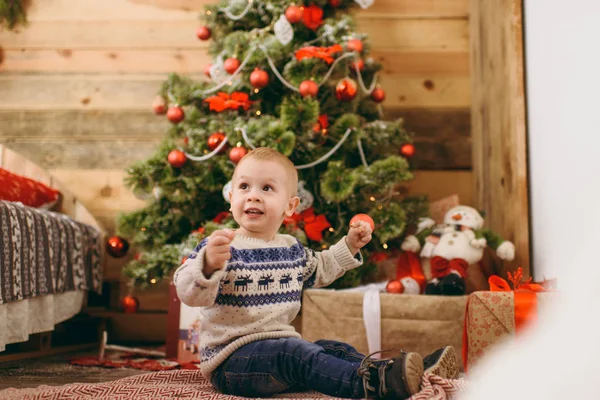 Feliz lindo niño vestido con suéter y jeans decorando el árbol de Navidad con juguetes en la habitación de madera en casa. Niño con buen humor. Año Nuevo. Estilo de vida, familia y vacaciones 2018 concepto — Foto de Stock
