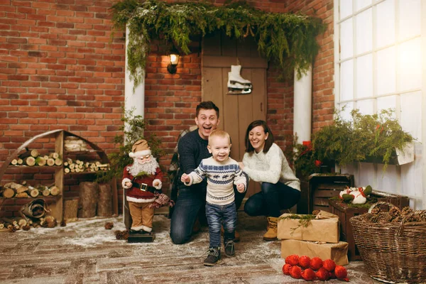 Μικρά χαρούμενα ευτυχείς γονείς με ένα χαριτωμένο μικρό παιδί αγόρι ντυμένος με πουλόβερ και τζιν στο διακοσμημένο νέο έτος της δωμάτιο με Santa στο σπίτι. Χριστούγεννα καλή διάθεση. Τρόπου ζωής, οικογένεια και διακοπές έννοια 2018 — Φωτογραφία Αρχείου