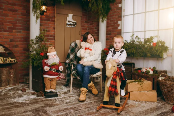 Νεαρή μητέρα ευτυχισμένος με χαριτωμένο μικρό παιδί αγόρι για κουνιστό άλογο στο διακοσμημένο νέο έτος της δωμάτιο με Santa στο σπίτι. Χριστούγεννα καλή διάθεση. Τρόπου ζωής, οικογένεια και διακοπές έννοια του 2018. Μαγικό κυριώτερη επίδραση — Φωτογραφία Αρχείου