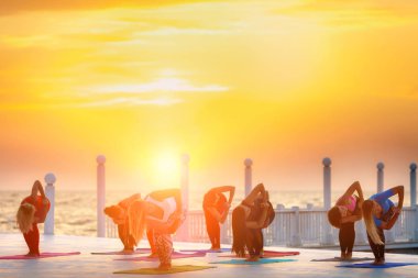 Bir grup kadın gündoğumu deniz kenarında, yoga yaparken