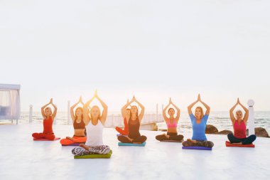 Bir grup kadın gündoğumu deniz kenarında, yoga yaparken