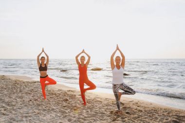 Bir grup kadın gündoğumu deniz kenarında, yoga yaparken