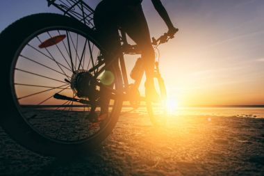 Suya yakın bir çöl bölgesinde bir bisikletle çok renkli elbiseli bir kadın oturuyor. Fitness kavramı. Arka görüş ve alt görüntüleyin. Yakın çekim