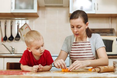 Küçük çocuk çocuk anne Noel ışık mutfakta zencefilli bisküvi pişirmek için yardımcı olur. Mutlu aile anne 30-35 yıl ve 2-3 rulo dışarı hamur ve çerezler de uygunbir çocuk ev. İlişki ve sevgi kavramı