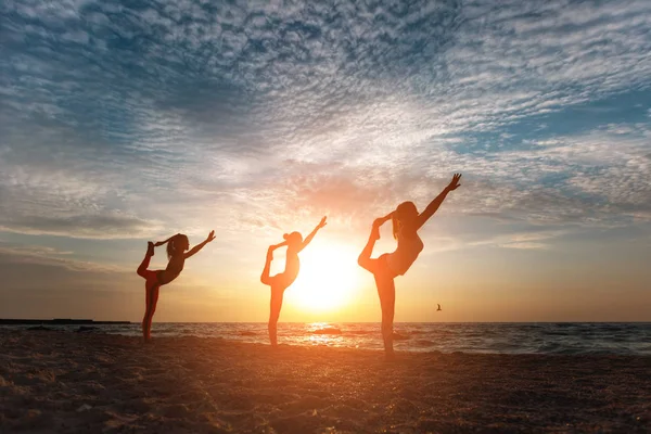 Bir grup kadın gündoğumu deniz kenarında, yoga yaparken — Stok fotoğraf