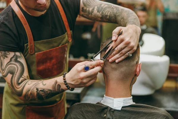 Nahaufnahme eines Mannes, der sich beim Friseur eine modische Frisur schneidet. männlicher Friseur mit Tätowierungen im Dienste des Kunden. — Stockfoto