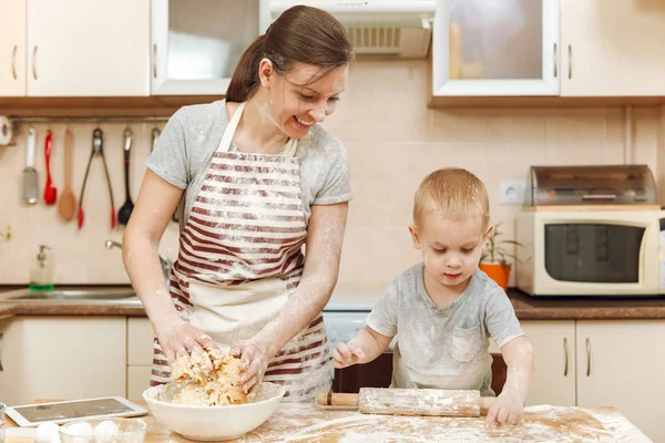 Маленький мальчик помогает маме готовить рождественское имбирное печенье на светлой кухне с табличкой на столе. Счастливая семейная мама 30-35 лет и ребенок 2-3 в выходные утром дома. Концепция отношений — стоковое фото