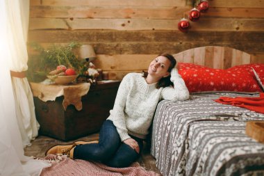 Güzel Avrupa genç kahverengi saçlı kadın ahşap rustik Oda evde yatakta katta oturan Kazak giymiş. Noel keyfi. Yeni yıl. Yaşam tarzı, Aile ve tatil 2018 kavramı