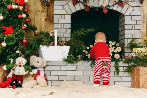 Retrato de juguetón niño lindo lindo bebé en ropa roja cerca de la chimenea en una habitación decorada en casa. Navidad buen humor. Año Nuevo. Concepto de estilo de vida, familia y unión . — Foto de Stock