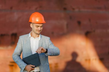 Güneşli bir günde liman kargo paslı gemi arka plan karşı takım, tablet, holding koruyucu inşaat turuncu kask yakışıklı tıraşsız başarılı iş adamı, nöbette seyir zaman ayakta