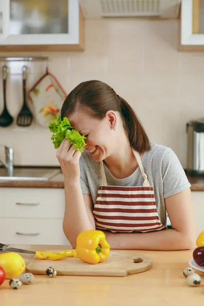 Молодая привлекательная женщина в фартуке с листьями салата, смеющаяся на кухне. Концепция диеты. Здоровый образ жизни. Готовить дома. Готовьте еду. . — стоковое фото