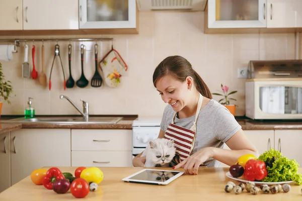 Una giovane bella donna con gatto bianco persiano in cucina con tablet sul tavolo. Insalata di verdure. Il concetto di dieta. Uno stile di vita sano. Cucinare a casa. Preparare il cibo . — Foto Stock