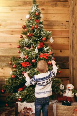 Mutlu sevimli küçük erkek bebek kazak ve ahşap Oda evde oyuncaklar ile Noel ağacı süsleme kot pantolon giymiş. Çocuk iyi bir ruh hali ile. Yeni yıl. Yaşam tarzı, Aile ve tatil 2018 kavramı