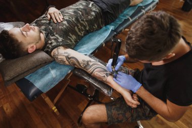 Profesyonel tattooer sanatçı tarafından makine siyah mürekkep bir kavanoz gelen adamın elini resim yapıyor. Vücudunda dövme sanatı. Dövme sanat yapmak için ekipman. Ana ışık studio dövmeli yapar.