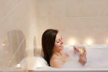 Uzun kahverengi saçlı ve düz çıplak vücut yalan, beyaz köpük küvet mum ışık banyoda, şarap cam kapalı içki alkol ile rahatlatıcı olan güzel seksi kadın.