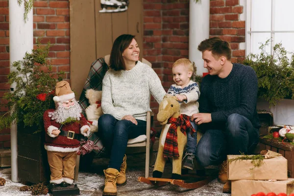 Młodzi rodzice zadowoleni z ładny mały chłopiec dziecko na koń na biegunach, ubrany w sweter w urządzonych pokojach nowy rok z Santa w domu. Dobry nastrój Bożego Narodzenia. Styl życia, rodziny i wakacje koncepcja 2018 — Zdjęcie stockowe