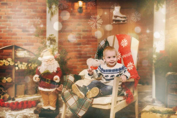 Niño niño feliz vestido con suéter sentado en la silla con Santa en la habitación decorada de Año Nuevo en casa. Navidad buen humor. Concepto familia y vacaciones 2018. Resalte mágico efecto bokeh — Foto de Stock