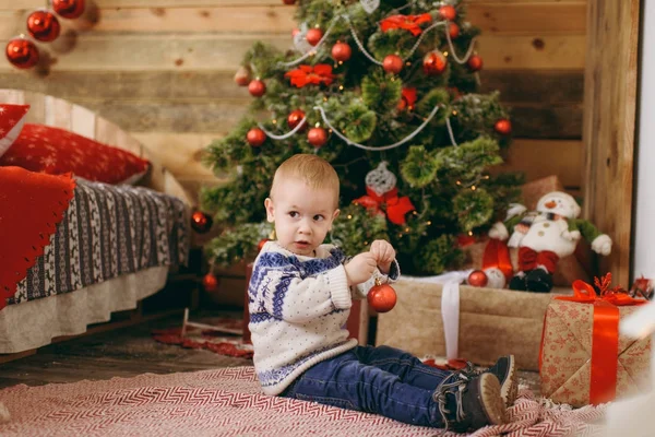 Feliz lindo niño vestido con suéter y jeans decorando el árbol de Navidad con juguetes en la habitación de madera en casa. Niño con buen humor. Año Nuevo. Estilo de vida, familia y vacaciones 2018 concepto — Foto de Stock