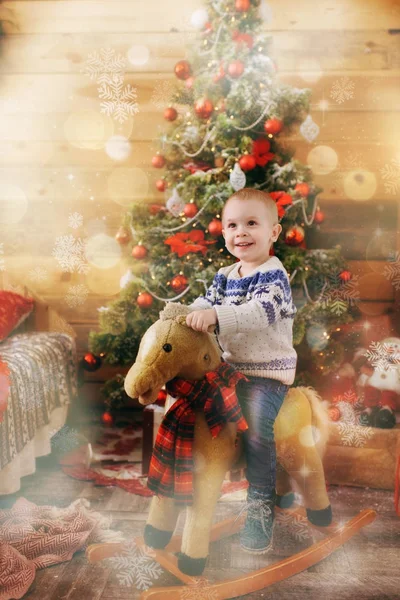 Feliz niño lindo en el caballo mecedora en el árbol de Navidad con un juguete en la habitación decorada de Año Nuevo en casa. Buen humor para niños. Estilo de vida, familia y vacaciones 2018 concepto. Efecto mágico resaltado — Foto de Stock