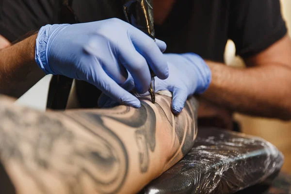 Close up of professional tattooer artist doing picture on hand of man by machine black ink from a jar. Tattoo art on body. Equipment for making tattoo art. Master makes tattooed in light studio. — Stock Photo, Image