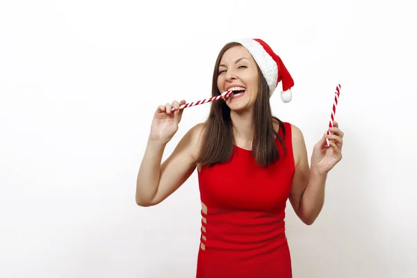 美丽的白种人年轻滑稽快乐的女人与迷人的笑容在红色的礼服和圣诞帽持有条纹棒糖在白色背景。孤立的圣诞老人女孩。新年假期2018概念 — 图库照片