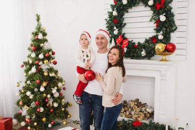 Şapkalı şirin küçük oğluyla mutlu anne. Büyük kırmızı Ağaç oyuncak topu ayakta dekore edilmiş yeni yıl ışık Oda evde Noel çelenk arka plan üzerinde çocuk çocuk. Aile, tatil 2018 kavramı.