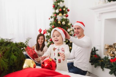 Şapkalı şirin küçük oğluyla mutlu anne. Büyük kırmızı Ağaç oyuncak topu ayakta dekore edilmiş yeni yıl ışık Oda evde çocuk çocuk. Noel keyfi. Aile, sevgi ve tatil 2018 kavramı.
