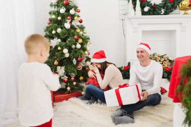 Mutlu neşeli anne ile şirin küçük oğlu kırmızı şapkalı. Çocuk çocuk odasında ışık evde yılbaşı ağacı ve hediye kutuları ile dekore edilmiştir. Noel keyfi. Aile, sevgi ve tatil 2018 kavramı.