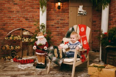 Oynak mutlu sevimli küçük çocuk çocuk kazak ve Noel Baba evde dekore edilmiş yeni yıl odasında sandalye üzerinde oturan kot pantolon giymiş. Noel keyfi. Yaşam tarzı, Aile ve tatil 2018 kavramı