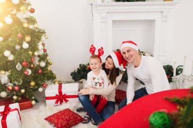 Sevimli küçük oğluyla mutlu neşeli anne. Kırmızı şapkalı dekore edilmiş yeni yıl ağacı ve hediye kutuları ile ışık Oda evde oturan çocuk çocuk. Noel keyfi. Aile, sevgi ve tatil 2018 kavramı.