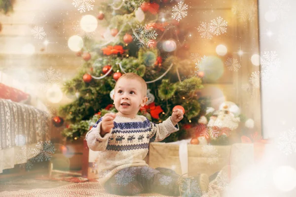 Niño pequeño y feliz vestido con jersey decorando el árbol de Navidad con juguetes en la habitación de madera en casa. Buen humor para niños. Año Nuevo. Estilo de vida, familia y vacaciones 2018 concepto. Efecto mágico resaltado — Foto de Stock