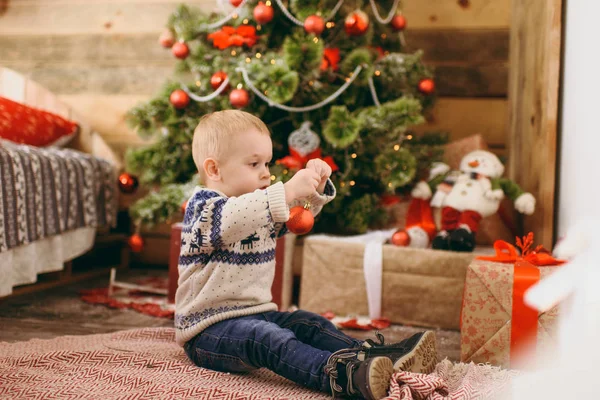 Feliz lindo niño vestido con suéter y jeans decorando el árbol de Navidad con juguetes en la habitación de madera en casa. Niño con buen humor. Año Nuevo. Estilo de vida, familia y vacaciones 2018 concepto — Foto de Stock