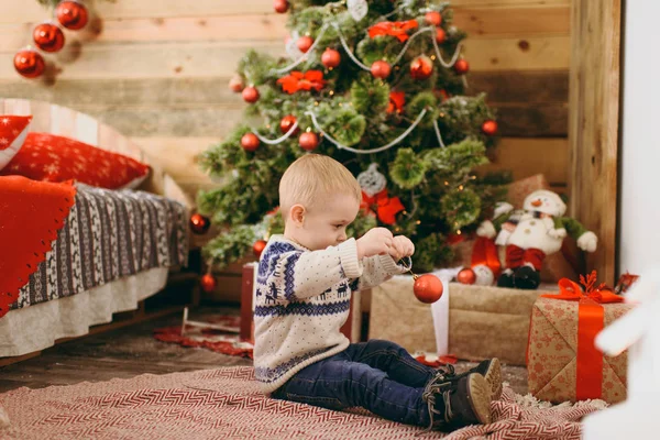 Feliz lindo niño vestido con suéter y jeans decorando el árbol de Navidad con juguetes en la habitación de madera en casa. Niño con buen humor. Año Nuevo. Estilo de vida, familia y vacaciones 2018 concepto — Foto de Stock