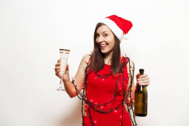 Güzel çekici genç gülümseyen mutlu kadın Kırmızı elbiseli, Noel şapka, cam ve şişe şampanya beyaz arka plan ayakta fenerler garland. Noel Baba kız izole. Yeni yıl 2018 tatil