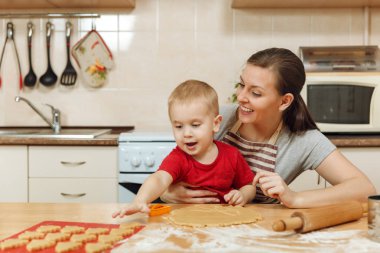 Küçük çocuk çocuk anne Noel ışık mutfakta zencefilli bisküvi pişirmek için yardımcı olur. Mutlu aile anne 30-35 yıl ve 2-3 rulo dışarı hamur ve çerezler de uygunbir çocuk ev. İlişki ve sevgi kavramı