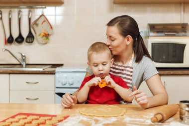Küçük çocuk çocuk anne Noel ışık mutfakta zencefilli bisküvi pişirmek için yardımcı olur. Mutlu aile anne 30-35 yıl ve 2-3 rulo dışarı hamur ve çerezler de uygunbir çocuk ev. İlişki ve sevgi kavramı
