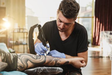 Profesyonel tattooer sanatçı tarafından makine siyah mürekkep bir kavanoz gelen adamın elini resim yapıyor. Vücudunda dövme sanatı. Dövme sanat yapmak için ekipman. Ana ışık studio dövmeli yapar.