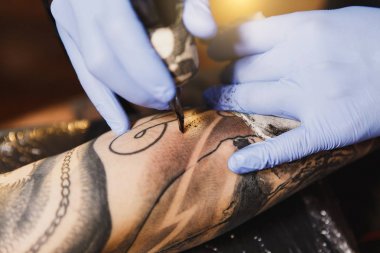 Profesyonel tattooer sanatçı tarafından makine siyah mürekkep bir kavanoz gelen adamın elini resim yapıyor kapatın. Vücudunda dövme sanatı. Dövme sanat yapmak için ekipman. Ana ışık studio dövmeli yapar.