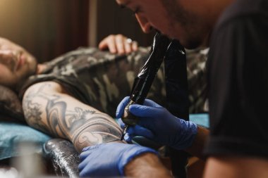 Profesyonel tattooer sanatçı tarafından makine siyah mürekkep bir kavanoz gelen adamın elini resim yapıyor kapatın. Vücudunda dövme sanatı. Dövme sanat yapmak için ekipman. Ana ışık studio dövmeli yapar.