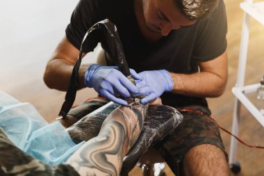 Profesyonel tattooer sanatçı tarafından makine siyah mürekkep bir kavanoz gelen adamın elini resim yapıyor. Vücudunda dövme sanatı. Dövme sanat yapmak için ekipman. Ana ışık studio dövmeli yapar.